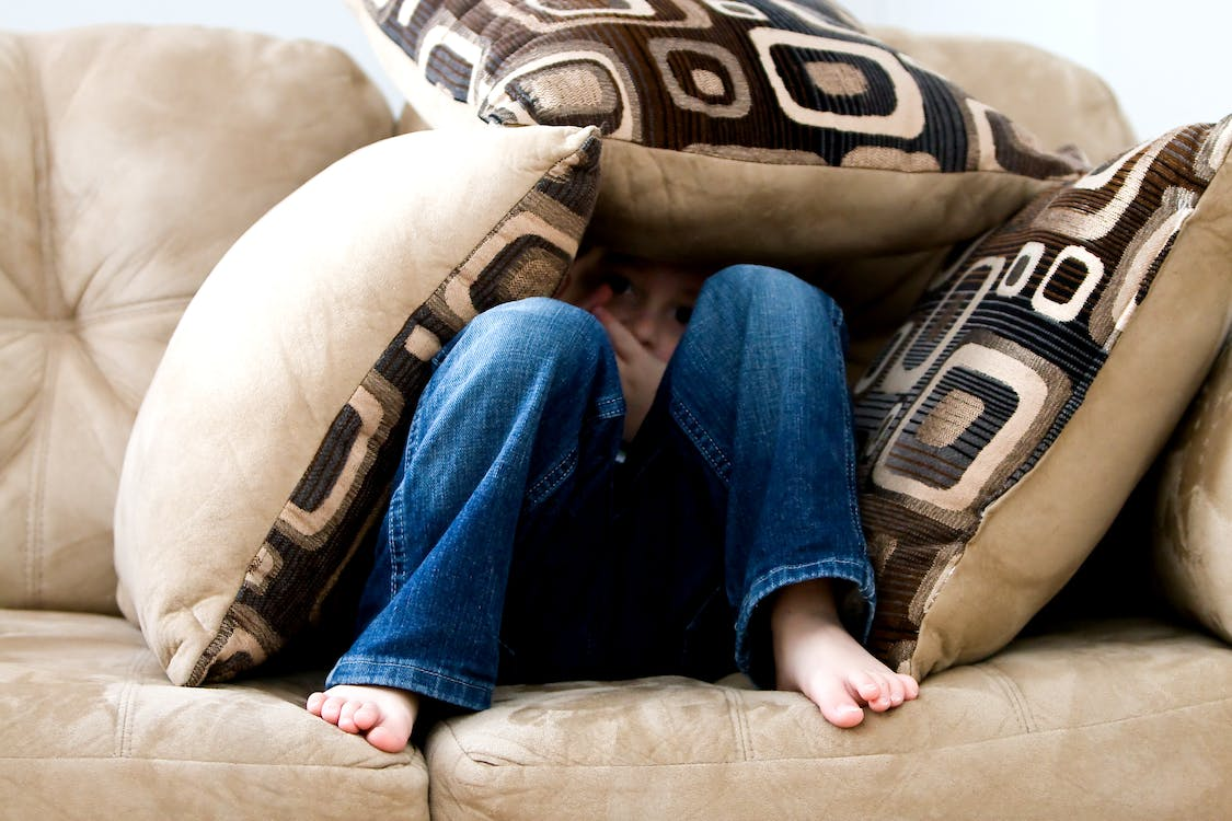Child hiding under cushions on a sofa, showcasing the emotional impact of domestic violence on minors.
