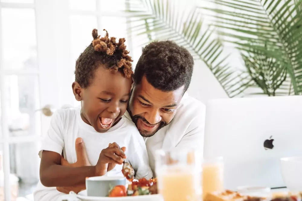 Joyful father and child sharing a light moment during breakfast.