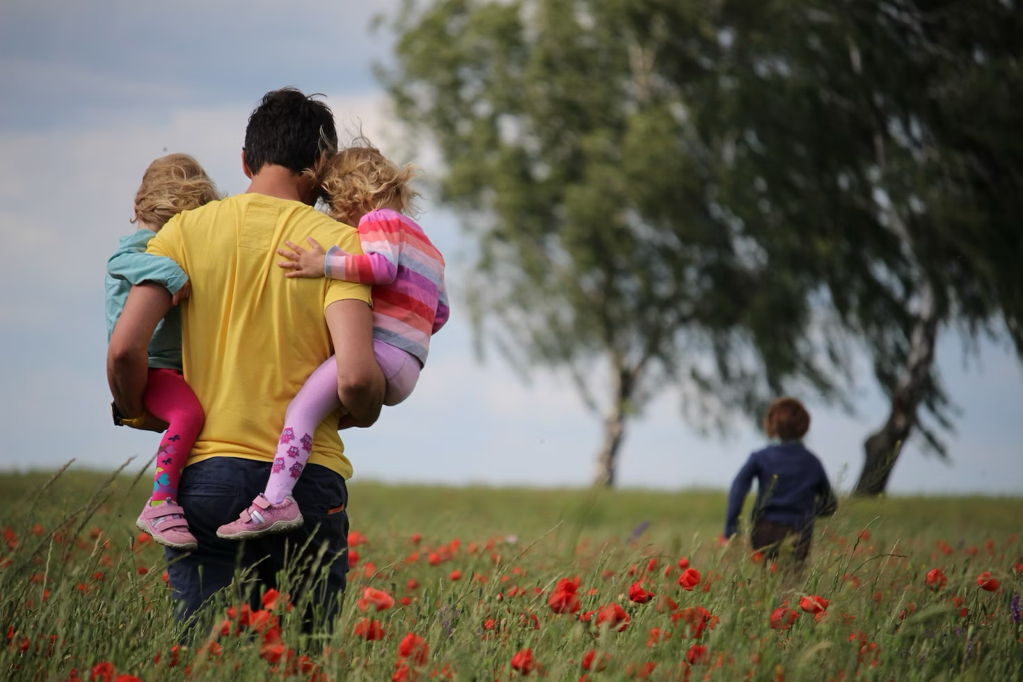 A father holding his daughters while his son frolics ahead