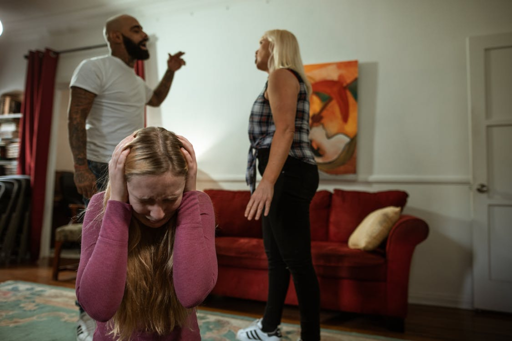 A child looking visibly upset while two adults argue in the background