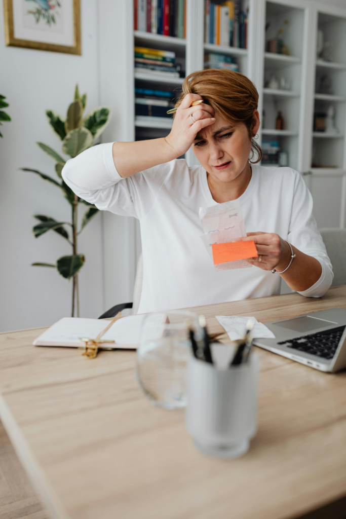 A worried woman looking at a receipt while holding her head