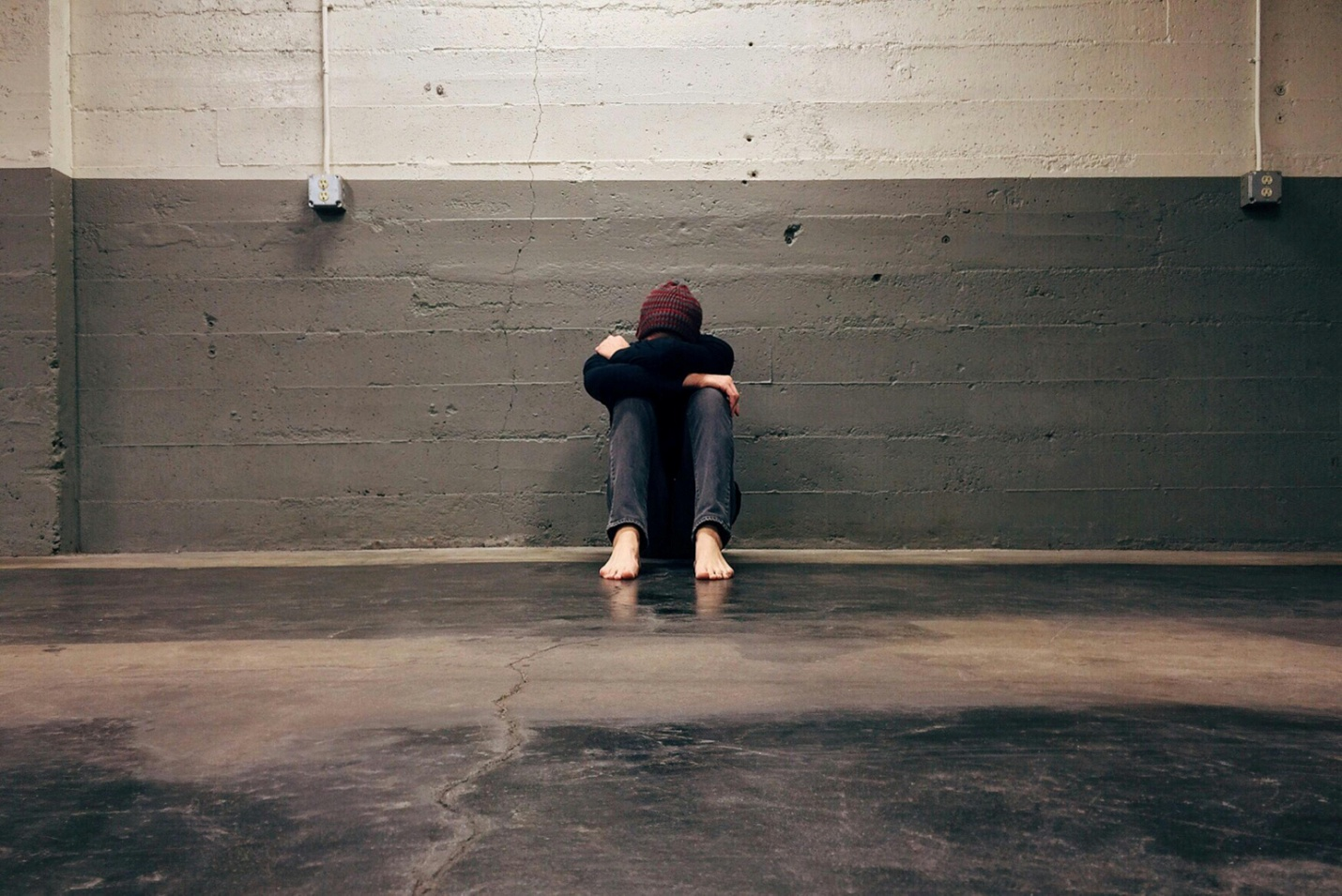 A depressed person sitting against a wall with his head in his arms
