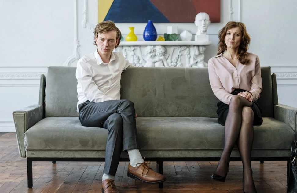 a couple sitting away from each other by https://www.pexels.com/photo/woman-in-white-dress-shirt-and-black-pants-sitting-on-gray-couch-4098205/