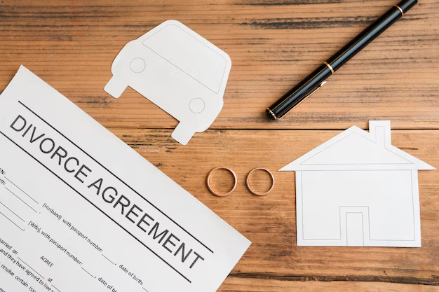 Divorce agreement with wedding rings, a pen, and cut-outs of a home and car symbolizing property division.