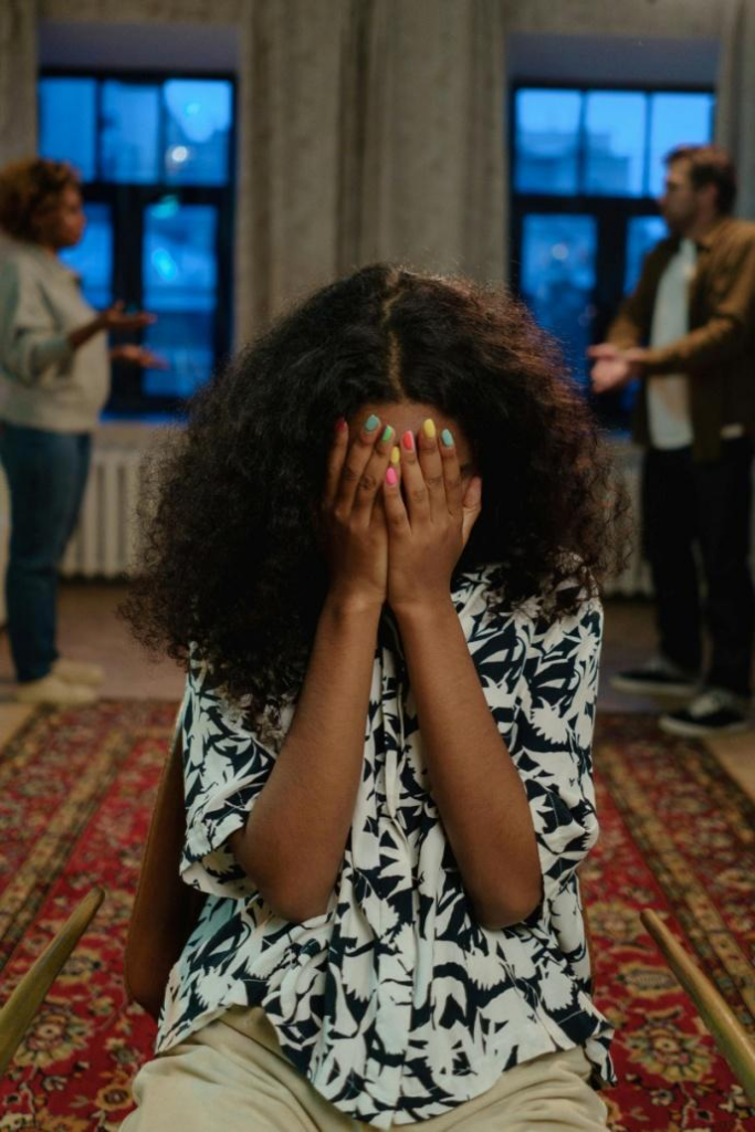 A picture of a child covering her face with her parents arguing behind