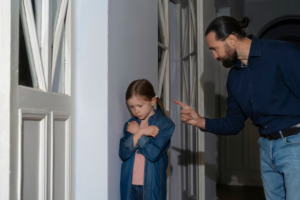 Child looking afraid as father scolds her, showing parental abuse as a factor in custody decisions