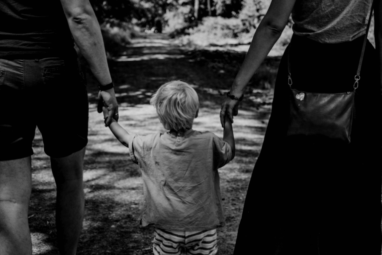 A monochrome picture of a kid holding his parents’ hands