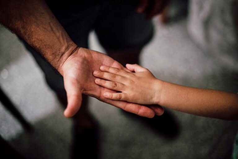 A child’s hand on top of a father’s hand