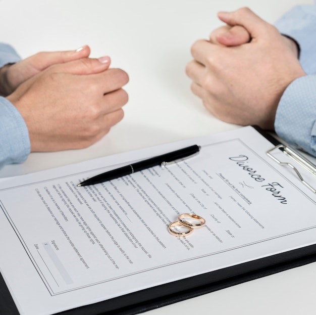 Two people with a divorce form and their wedding rings on it