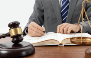 Person writing in a legal book with a gavel on the table