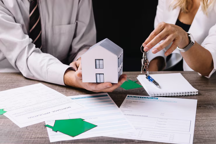 A man holding a miniature house while another person holds a set of keys