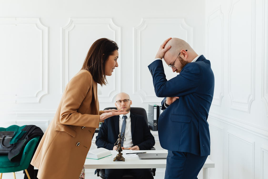 A frustrated couple arguing in front of their divorce lawyer during a delayed legal meeting