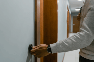 a person in a grey shirt ringing the doorbell of an apartment