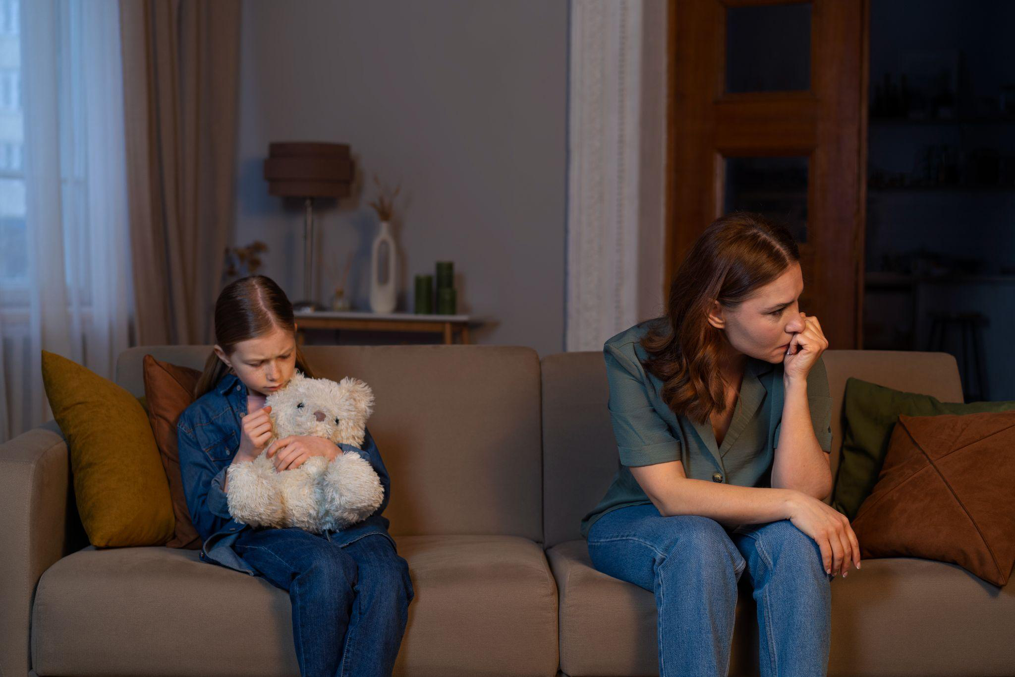 an upset child holding a toy, sitting at a distance from a crying mother