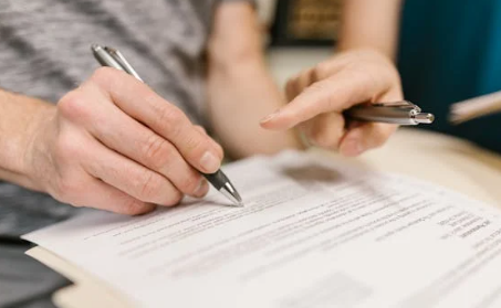 Close-up of two people reviewing and pointing at a legal document with pens.
