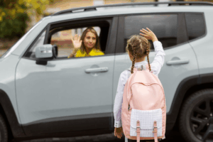 a woman in a car and a kid with a bag waving at each other