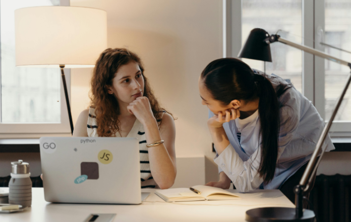 Two women having a serious discussion at a desk with a laptop.