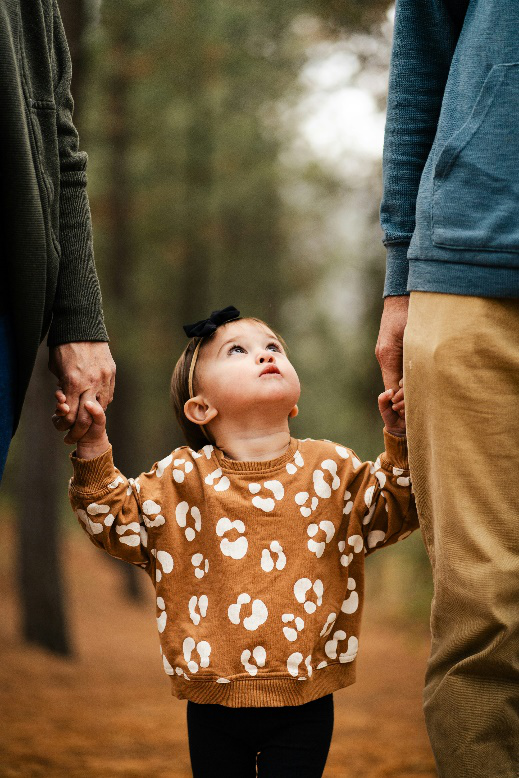 A little girl holding the hands of two people