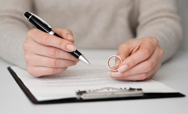 A woman signing divorce papers while holding her wedding ring