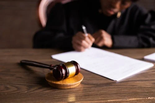 A person signing documents at a desk with a gavel in front