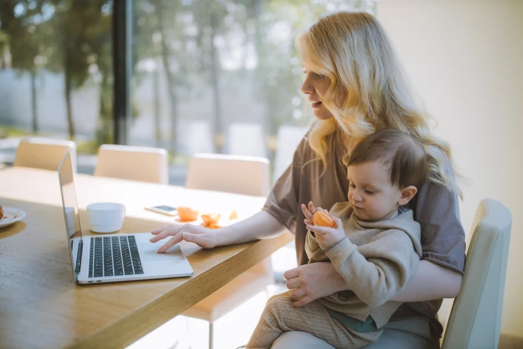 Mother holding her baby while working on a laptop, symbolizing CPS cases and custody issues handled by Montopolis family lawyers