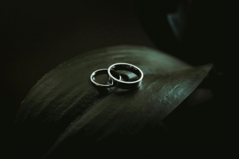 Two wedding rings resting on a dark leaf.