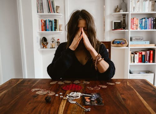 A woman holding her head with photos and a broken heart on the table.