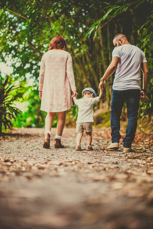 A child holding hands with two adults while walking on a pathway outdoors