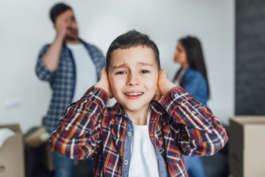  A boy with his hands on his ears while his parents quarrel in the background