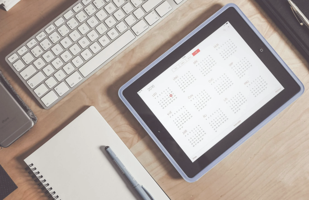 This photo shows a tablet screen displaying a calendar with a notebook and pen beside it.