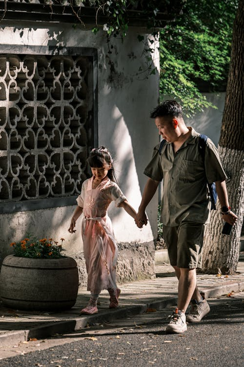 A father and young daughter walking hand in hand on a sunny sidewalk