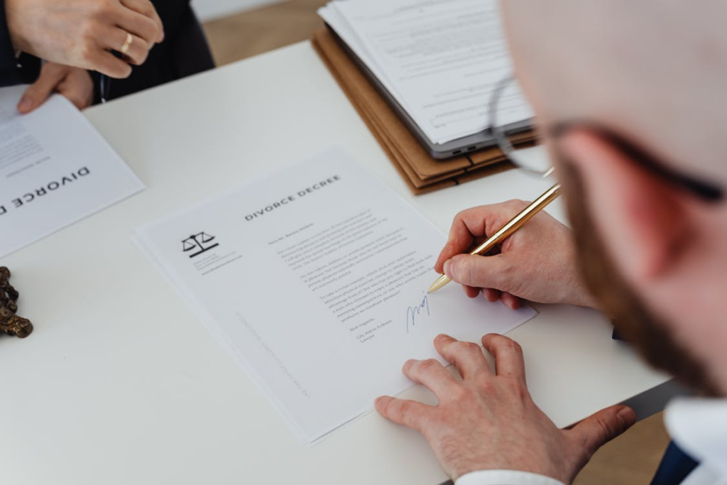 A person signing legal documents on a desk with a pen