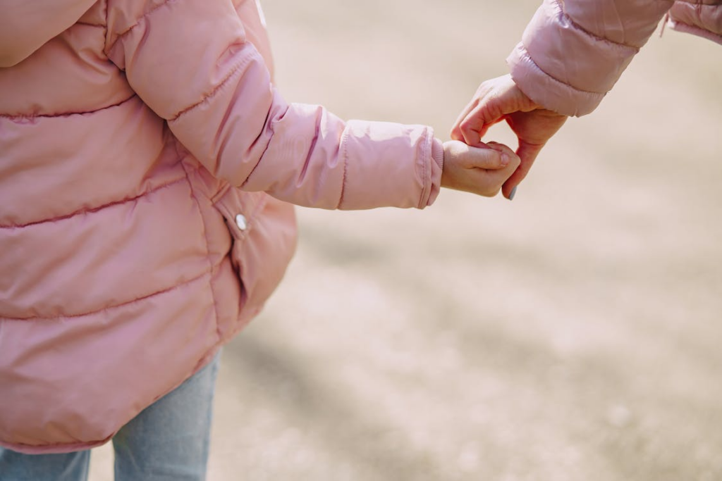 A parent and child in a pink jacket holding hands