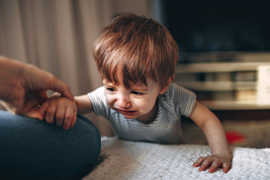 close-up of a little boy crying, trying to get on the bed to his parent