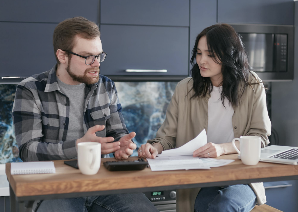 This photo shows a couple sitting at a table talking with papers nearby.