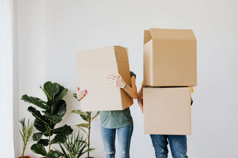 Two people carrying cardboard boxes into a living room