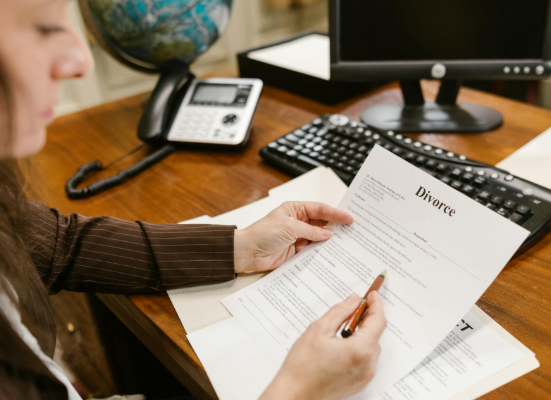 This image shows a woman reviewing divorce paperwork at an office desk.
