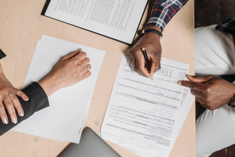 Two people signing documents at an office desk