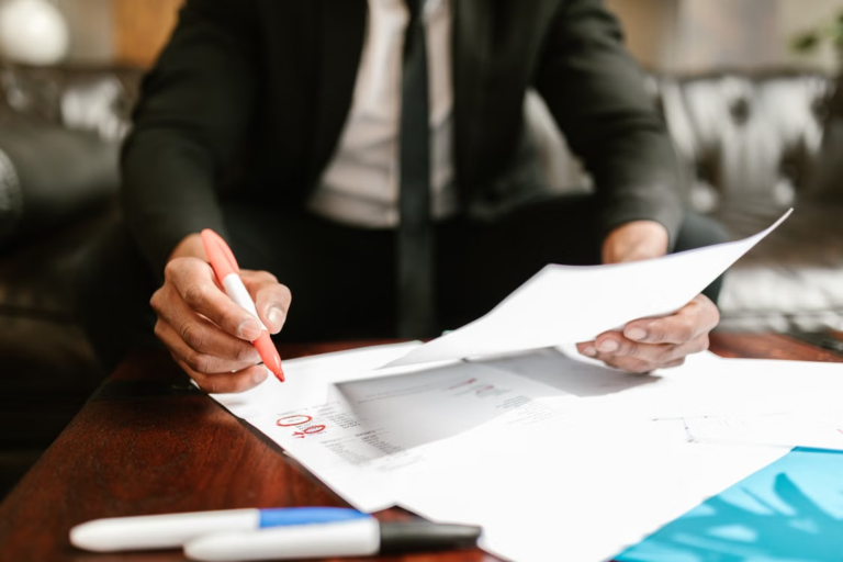 Person in a suit circling items in red ink on documents spread across a coffee table