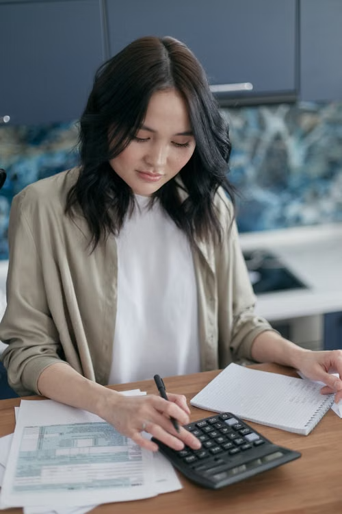 This image shows a woman using a calculator while reviewing bills at a desk.