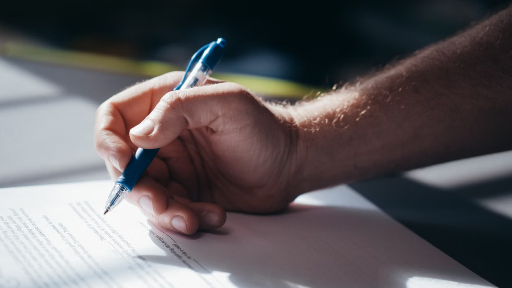 This image shows a close-up of a hand signing a document with a pen.