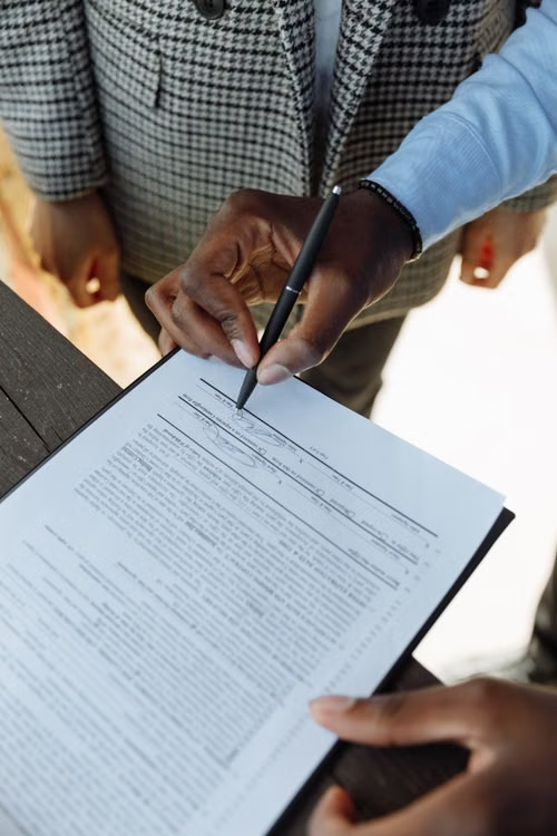 This image shows a close-up of a hand signing a contract with a pen.