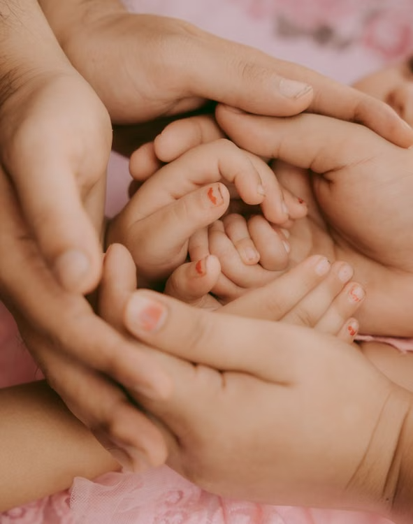 This image shows the hands of two adults gently holding a child's hands.