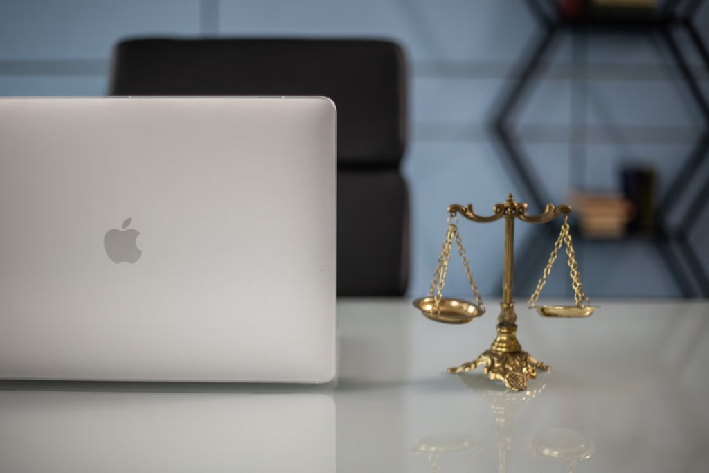 Laptop beside a set of brass scales of justice on a desk.