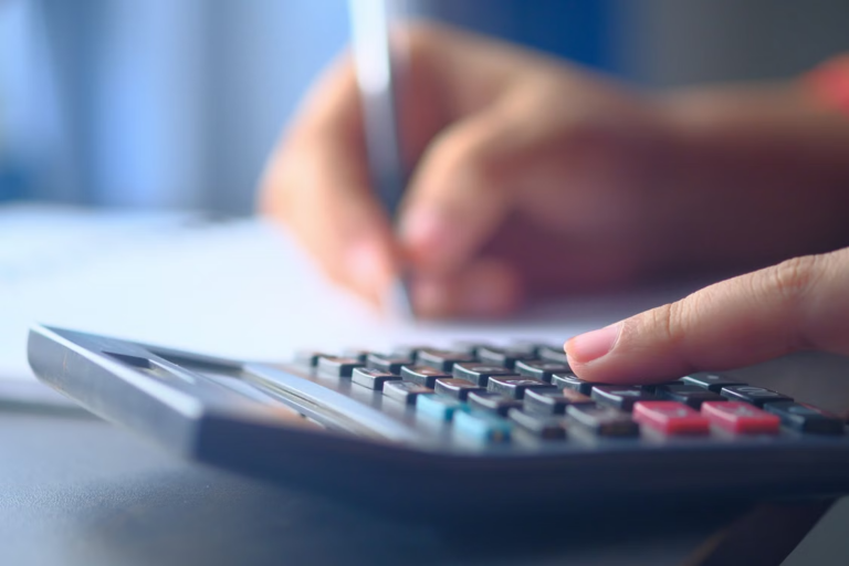 Person using a calculator beside documents on a desk.