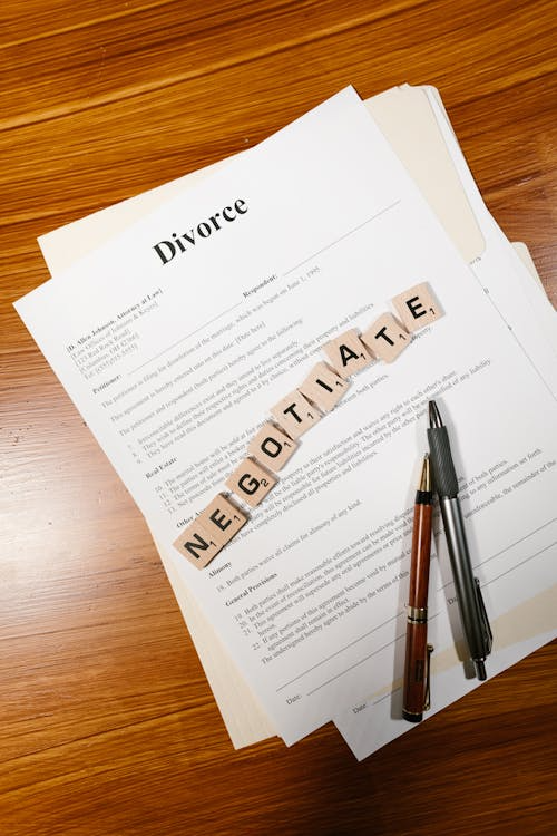 Divorce papers on a table, and the word ' negotiate’ written with tiles.
