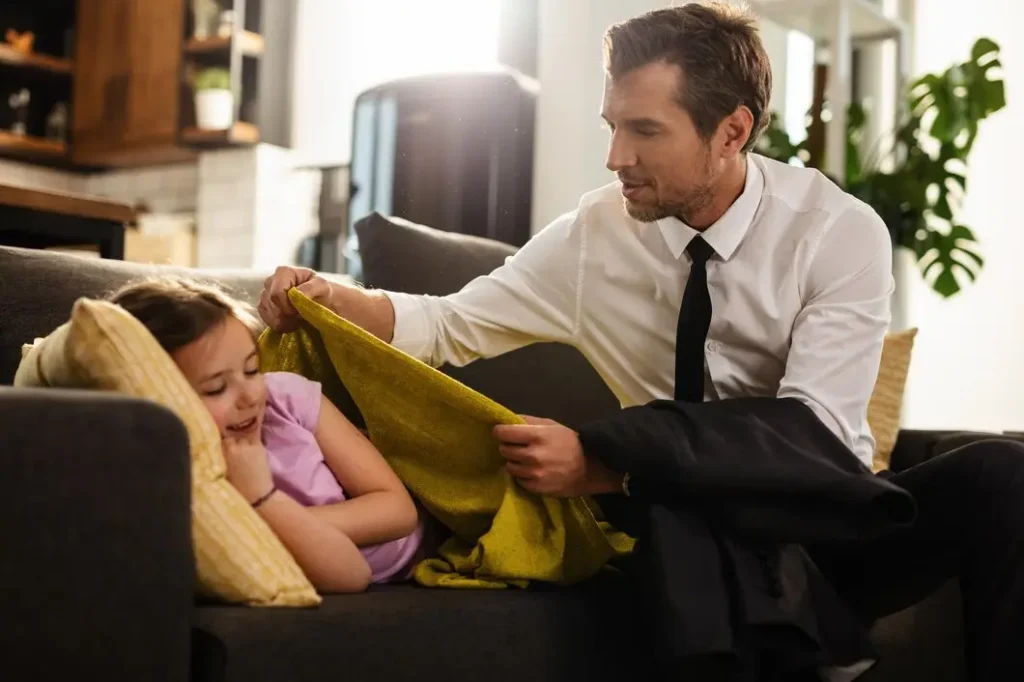 little girl lying down sofa while her father is covering her with blanket before going work focus