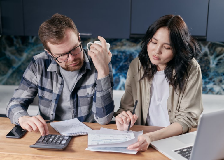 A couple reviewing bills and using a calculator at their kitchen table
